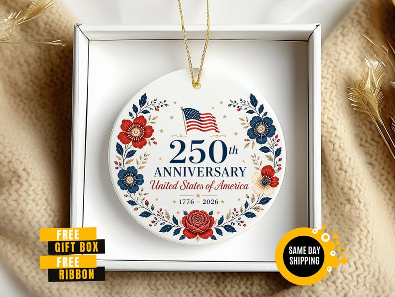 May include: A white ceramic ornament commemorating the 250th anniversary of the United States of America. The design features the American flag, floral elements in red and blue, and the text "250th Anniversary United States of America 1776-2026".