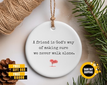 May include: A white ceramic ornament with the text "A friend is God's way of making sure we never walk alone." A red heart-shaped tree is below the text. The ornament has a brown string for hanging.
