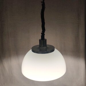 May include: A pendant light fixture with a white, rounded glass shade. The shade is suspended by a black cord and a metal fixture. The light is turned on, illuminating the shade.