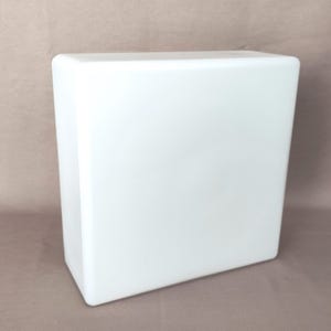 Könnte beinhalten: Ein weißes, rechteckiges Objekt mit abgerundeten Ecken. Das Objekt hat eine glatte, glänzende Oberfläche. Der Hintergrund ist eine neutrale, beige Farbe. Das Objekt scheint aus einem festen Material zu bestehen.