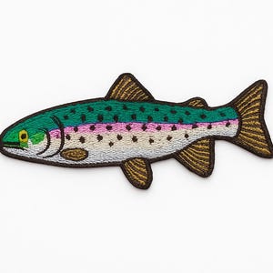 May include: Embroidered patch of a rainbow trout. The fish has a green back with black dots, a pink and white stripe, and gold fins. The patch is on a white background.