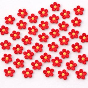 Puede incluir: Una colección de pequeñas flores rojas bordadas con centros amarillos. Las flores están dispuestas sobre una superficie blanca. Estos adornos florales decorativos son adecuados para varios proyectos de manualidades.