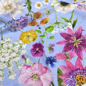 Peut inclure: Un tissu bleu clair avec un motif floral &agrave; l'aquarelle. Le motif pr&eacute;sente une vari&eacute;t&eacute; de fleurs dans les tons de rose, de violet, de jaune et de blanc, avec des feuilles vertes. Les fleurs sont dispers&eacute;es sur le tissu.