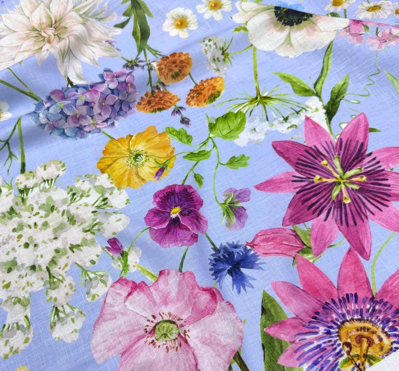 Peut inclure: Un tissu bleu clair avec un motif floral &agrave; l'aquarelle. Le motif pr&eacute;sente une vari&eacute;t&eacute; de fleurs dans les tons de rose, de violet, de jaune et de blanc, avec des feuilles vertes. Les fleurs sont dispers&eacute;es sur le tissu.