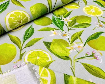 May include: Fabric with a light blue background featuring a pattern of green limes, lime slices, white blossoms, and green leaves. The limes are in various sizes and orientations, with some sliced to reveal the juicy interior. The fabric is folded, showing the texture and pattern.
