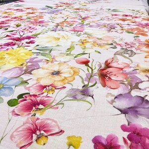 May include: A floral fabric featuring a vibrant array of flowers in shades of pink, yellow, purple, and orange. The design includes large blooms and smaller blossoms, creating a colorful and detailed pattern. The fabric has a light background.
