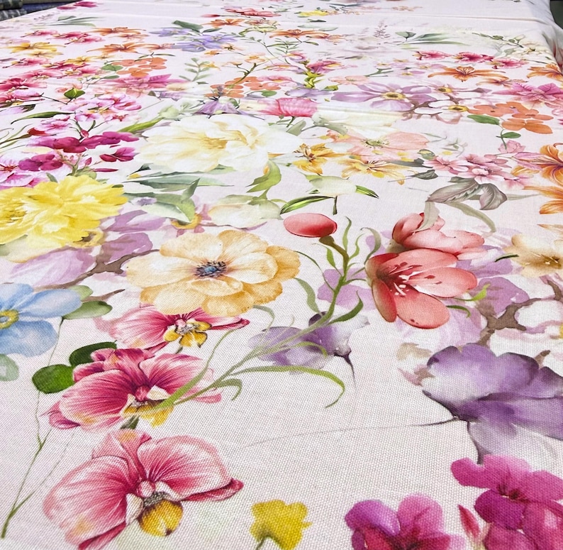 May include: A floral fabric featuring a vibrant array of flowers in shades of pink, yellow, purple, and orange. The design includes large blooms and smaller blossoms, creating a colorful and detailed pattern. The fabric has a light background.