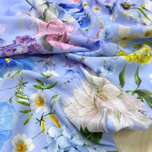 Peut inclure: Un tissu bleu clair avec un motif floral. Le motif pr&eacute;sente une vari&eacute;t&eacute; de fleurs dans les tons de rose, de violet, de blanc et de jaune. Le tissu est drap&eacute;, montrant la texture et le mouvement du mat&eacute;riau.