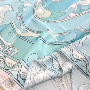 May include: A length of fabric featuring a repeating pattern of flowing, organic shapes in shades of light blue, teal, white, and soft pink. The design includes curved lines, circular motifs, and wave-like forms with distinct black outlines.