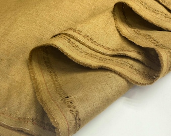 May include: Close-up of a folded piece of tan-colored fabric. The fabric has a textured appearance with visible fibers and a slightly frayed edge. The material appears to be a natural fiber, possibly linen or a similar textile.