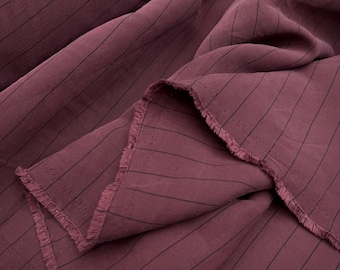 May include: A deep burgundy fabric featuring thin, vertical black pinstripes. The material is draped in soft folds, revealing a raw, frayed edge along the bottom border with visible small perforations along the selvage of the textile.