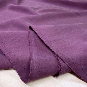 May include: A deep purple fabric with a visible woven texture and a frayed edge. The material features a distinct selvage border marked by a series of small, evenly spaced pinholes running along the length of the folded textile piece.