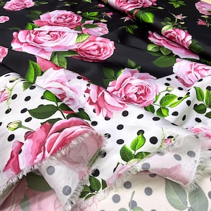 Puede incluir: Tela con estampado floral de rosas. La tela presenta grandes rosas rosas con hojas verdes sobre un fondo negro y un fondo blanco con lunares negros. La tela está doblada, mostrando los diferentes patrones.