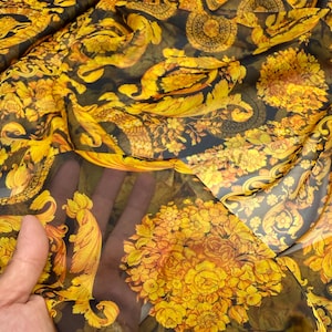 May include: A sheer, lightweight fabric featuring a vibrant yellow and gold baroque-inspired floral pattern printed over a dark, semi-transparent black background. The design includes intricate swirling acanthus leaves and dense clusters of roses.