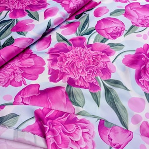 Puede incluir: Tela con estampado floral con grandes y vibrantes peonías rosas. El diseño incluye hojas verdes y pétalos rosas sobre un fondo azul claro y blanco. La tela está doblada, mostrando la repetición del patrón.