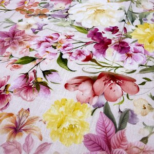 May include: A close-up of a floral pattern featuring a variety of flowers in shades of pink, yellow, and purple. The flowers are arranged on a light-colored background, creating a soft and delicate aesthetic. The design is reminiscent of a watercolor painting.