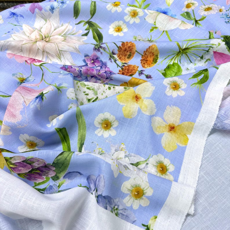 Peut inclure: Tissu floral bleu clair avec une vari&eacute;t&eacute; de fleurs blanches, jaunes, roses, violettes et oranges. Le tissu a une bordure blanche et un motif floral d&eacute;taill&eacute;. Les fleurs comprennent des marguerites, des dahlias et d'autres fleurs sauvages.