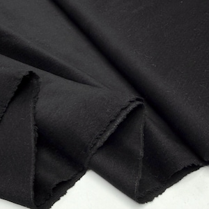 May include: A close-up shot of a folded piece of black fabric. The fabric has a soft, textured appearance and a raw, unfinished edge. The folds create shadows and depth, highlighting the material's texture.