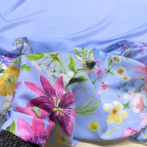 Peut inclure: Un tissu bleu clair orn&eacute; d'un motif floral. Le motif pr&eacute;sente de grandes fleurs roses et violettes, ainsi que de plus petites fleurs jaunes, blanches et roses. Des feuilles vertes sont parsem&eacute;es dans le motif. Le tissu est drap&eacute;, montrant le c&ocirc;t&eacute; &agrave; motifs et un fond bleu clair uni.