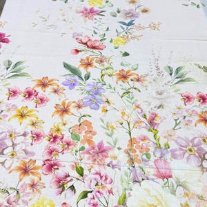 May include: A floral fabric featuring a watercolor design of various flowers in shades of pink, orange, yellow, and purple. The flowers are arranged on a white background with green leaves, creating a vibrant and colorful pattern.