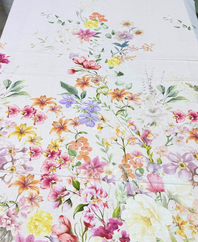 May include: A floral fabric featuring a watercolor design of various flowers in shades of pink, orange, yellow, and purple. The flowers are arranged on a white background with green leaves, creating a vibrant and colorful pattern.