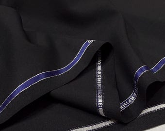 May include: Close-up of a folded black fabric with a subtle sheen. The fabric has a blue and white striped edge with text. The material appears to be high-quality, possibly for tailoring or fashion design.