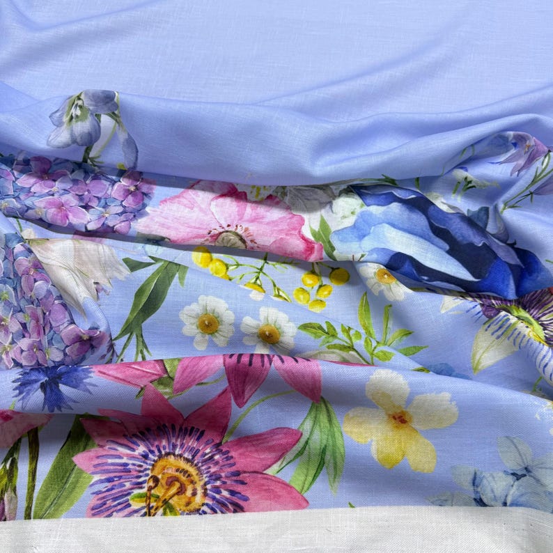 Peut inclure: Un tissu bleu clair orn&eacute; d'un imprim&eacute; floral vibrant. Le motif pr&eacute;sente une vari&eacute;t&eacute; de fleurs dans des tons de rose, violet, bleu, jaune et blanc. Le tissu est probablement du lin ou une mati&egrave;re l&eacute;g&egrave;re similaire, adapt&eacute; &agrave; l'habillement ou &agrave; la d&eacute;coration int&eacute;rieure.