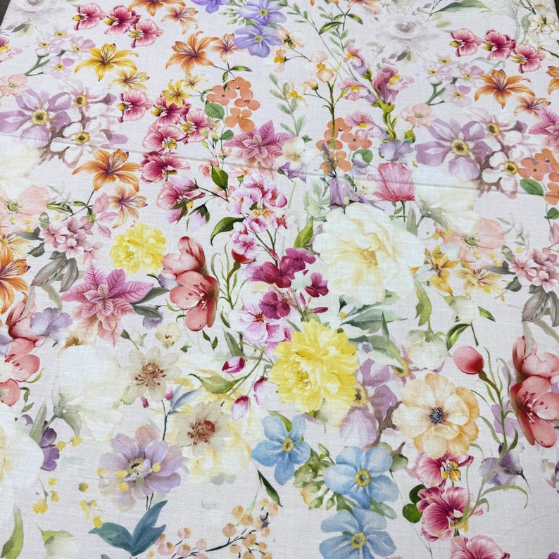 May include: A fabric with a vibrant floral pattern. The design features a variety of flowers in shades of pink, yellow, orange, purple, and blue, set against a light background. The flowers are detailed and realistic, creating a colorful and lively textile.
