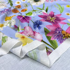 Peut inclure: Un tissu bleu clair orn&eacute; d'un motif floral vibrant. Le design pr&eacute;sente diverses fleurs aux tons de rose, violet, jaune et blanc, avec des feuilles vertes. Le tissu a un bord blanc non fini, sugg&eacute;rant une pi&egrave;ce coup&eacute;e.