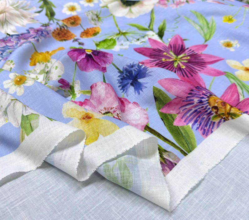 Peut inclure: Un tissu bleu clair orn&eacute; d'un motif floral vibrant. Le design pr&eacute;sente diverses fleurs aux tons de rose, violet, jaune et blanc, avec des feuilles vertes. Le tissu a un bord blanc non fini, sugg&eacute;rant une pi&egrave;ce coup&eacute;e.