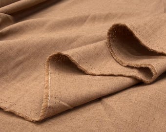 May include: Close-up of a tan-colored fabric with a textured weave. The fabric is folded, revealing a raw edge with white stitching. The material appears to be linen or a similar natural fiber, suitable for apparel or home decor.
