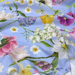 Peut inclure: Gros plan sur un tissu bleu clair orn&eacute; de motifs floraux aux couleurs rose, jaune, blanc et violet. Le tissu pr&eacute;sente une texture de type lin et une bordure blanche.