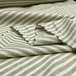 May include: Close-up of a folded fabric with a cream-colored background and green stripes. The stripes run diagonally across the fabric. The edges of the fabric are frayed, revealing the green thread. The fabric appears to be a woven material.