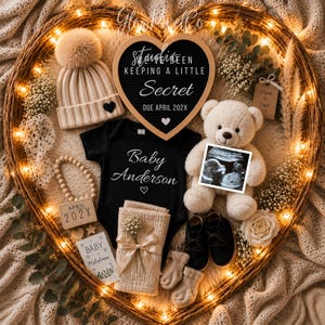Könnte beinhalten: Ein herzförmiger Weidenkorb mit Lichterketten, der Baby-Ankündigungsartikel enthält. Enthält eine beige Strickmütze, einen schwarzen Body mit "Baby Anderson", einen Teddybär mit Ultraschallbild und ein Schild mit der Aufschrift "Secret".