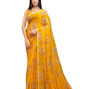 May include: A woman wearing a flowing, yellow saree with a floral pattern. The saree is a vibrant shade of yellow and features a repeating design of large, stylized flowers in a lighter, muted tone. The fabric drapes elegantly.