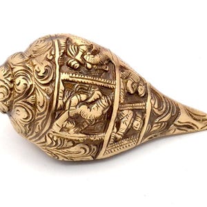 May include: A white ceramic mug with a black handle and the text "But First, Coffee" in a bold, black font. The mug is set against a blurred background, suggesting a cozy setting.