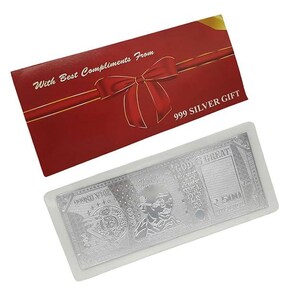 Puede incluir: Un regalo de plata con forma de billete de ₹500, dentro de una funda transparente, acompañado de una tarjeta roja con un lazo y el texto "With Best Compliments From" y "999 SILVER GIFT".