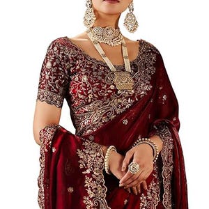 Puede incluir: Un sari granate con bordados dorados y una blusa a juego. El conjunto se complementa con un collar, pendientes y una diadema dorados. Un anillo y pulseras doradas completan el look. El sari es una prenda tradicional india.
