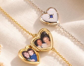May include: Two heart-shaped lockets on delicate chains. One silver locket is closed and features a small blue stone. The other gold locket is open, revealing two interior photographs: one showing an older couple and the other showing a woman holding a child.