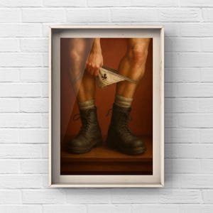 Op de afbeelding: Ingelijst kunstwerk met de benen van een persoon, die zwarte laarzen en grijze sokken draagt. De persoon houdt een witte onderbroek met een klein zwart ontwerp omhoog. De achtergrond is een warme, roodachtig bruine kleur.