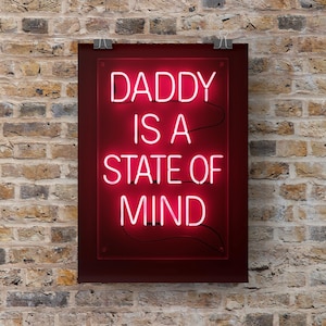 Könnte beinhalten: Rotes Neon-Schild mit dem Text "DADDY IS A STATE OF MIND" in weißer Schrift. Das Schild ist auf einer dunkelroten rechteckigen Platte montiert und vor einer Backsteinmauer aufgehängt.