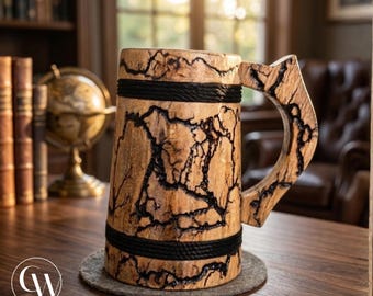 Può includere: Un boccale cilindrico in legno con finitura in venature di legno naturale color marrone chiaro e motivi di bruciatura frattale scuri e ramificati sulla superficie. Il boccale include due fasce orizzontali nere e un manico in legno angolare.