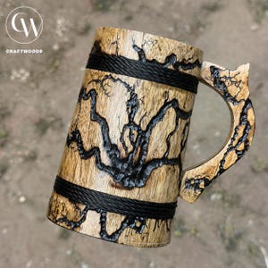 Pu&ograve; includere: Un boccale in legno caratterizzato da intricati motivi di bruciatura frattale nera sulla superficie. Il corpo cilindrico &egrave; accentuato da due fasce orizzontali in corda nera e include un manico in legno abbinato con un'estensione superiore a punta.