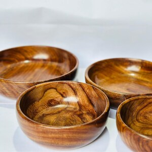 May include: Four wooden bowls with a rich, warm brown color and visible wood grain. The bowls are round with a smooth, polished finish. The bowls are nested together, showcasing their varying sizes and natural wood patterns.