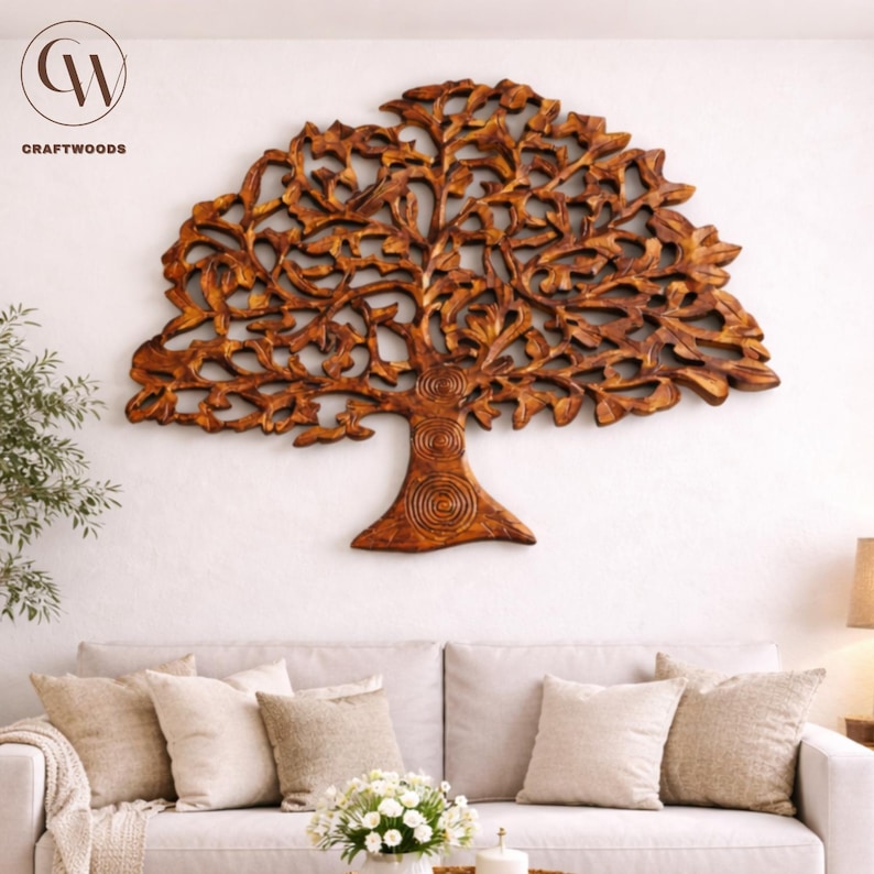 May include: A large, intricately carved wooden tree wall art piece. The tree is a warm brown colour, with detailed leaves and branches. The Craftwoods logo is in the upper left corner. The art is mounted on a white wall above a sofa with neutral-coloured cushions.