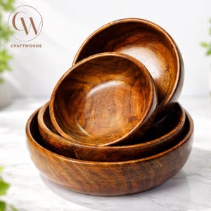 May include: A stack of four wooden bowls in varying sizes, showcasing a rich, warm brown hue. The bowls are nested together, revealing the natural wood grain. The Craftwoods logo is visible in the upper left corner.
