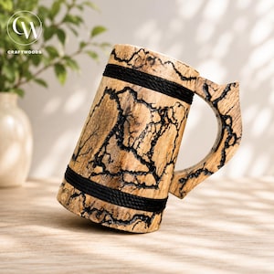 Pu&ograve; includere: Un boccale in legno caratterizzato da una finitura color legno naturale chiaro con motivi di bruciatura frattali scuri e ramificati sulla superficie. Il boccale &egrave; accentuato da due fasce orizzontali in corda nera avvolte attorno alla base e alla parte superiore.