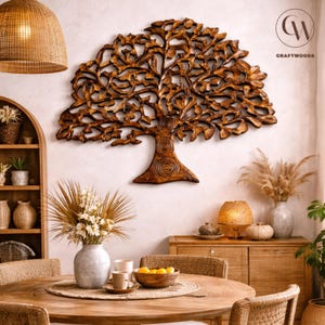 May include: A detailed wooden tree sculpture, mounted on a white wall. The tree features an intricate design of leaves and branches. The room is decorated with a round wooden table, vases, lamps, and other decorative items, creating a warm atmosphere.