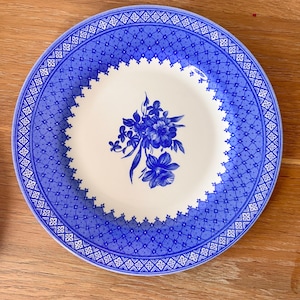 Op de afbeelding: Een ronde, wit en blauwe decoratieve plaat. De plaat heeft een blauw bloemmotief in het midden en een blauw patroonrand. De plaat is gemaakt van keramiek en is geschikt voor het serveren van voedsel.