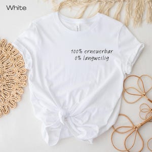 Puede incluir: Camiseta blanca con el texto "100% erneuerbar 0% langweilig" en escritura negra. La camiseta est&aacute; anudada a la cintura. La camiseta est&aacute; sobre una superficie blanca con elementos decorativos.